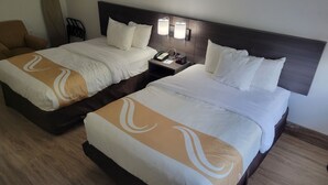A hotel room with two beds, each with white bedding and a brown design. There is a nightstand with a phone and a clock.