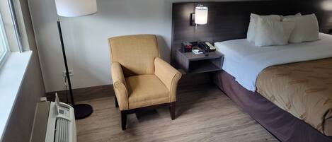 Una habitación de hotel con una cama, una silla, una mesita de noche con teléfono, una lámpara y un radiador.