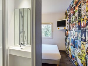 Un baño moderno con mampara de vidrio, un lavabo blanco, una mesita de noche pequeña y una pared decorada con carteles de viaje.