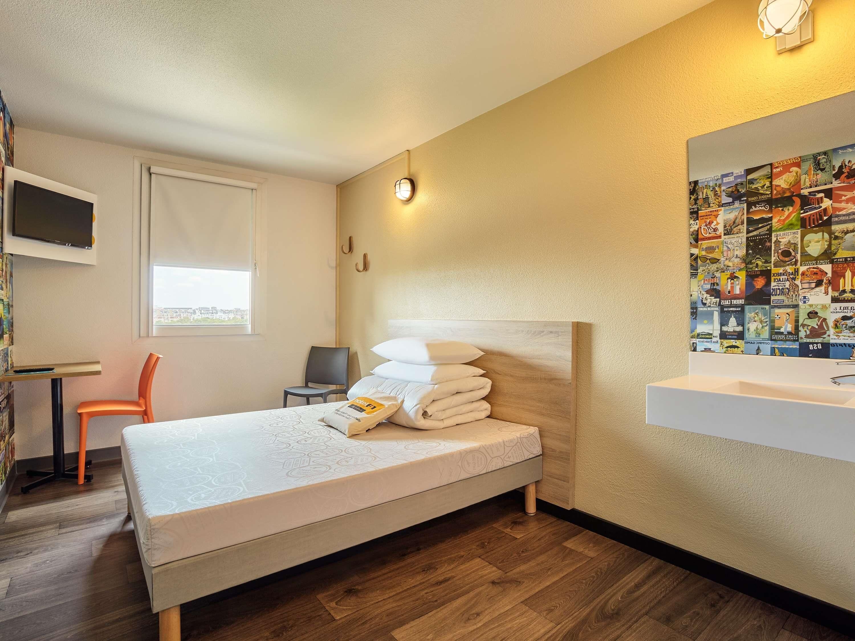 Un dormitorio ordenado con cama, escritorio, silla, televisor y una pared decorada con varios carteles.