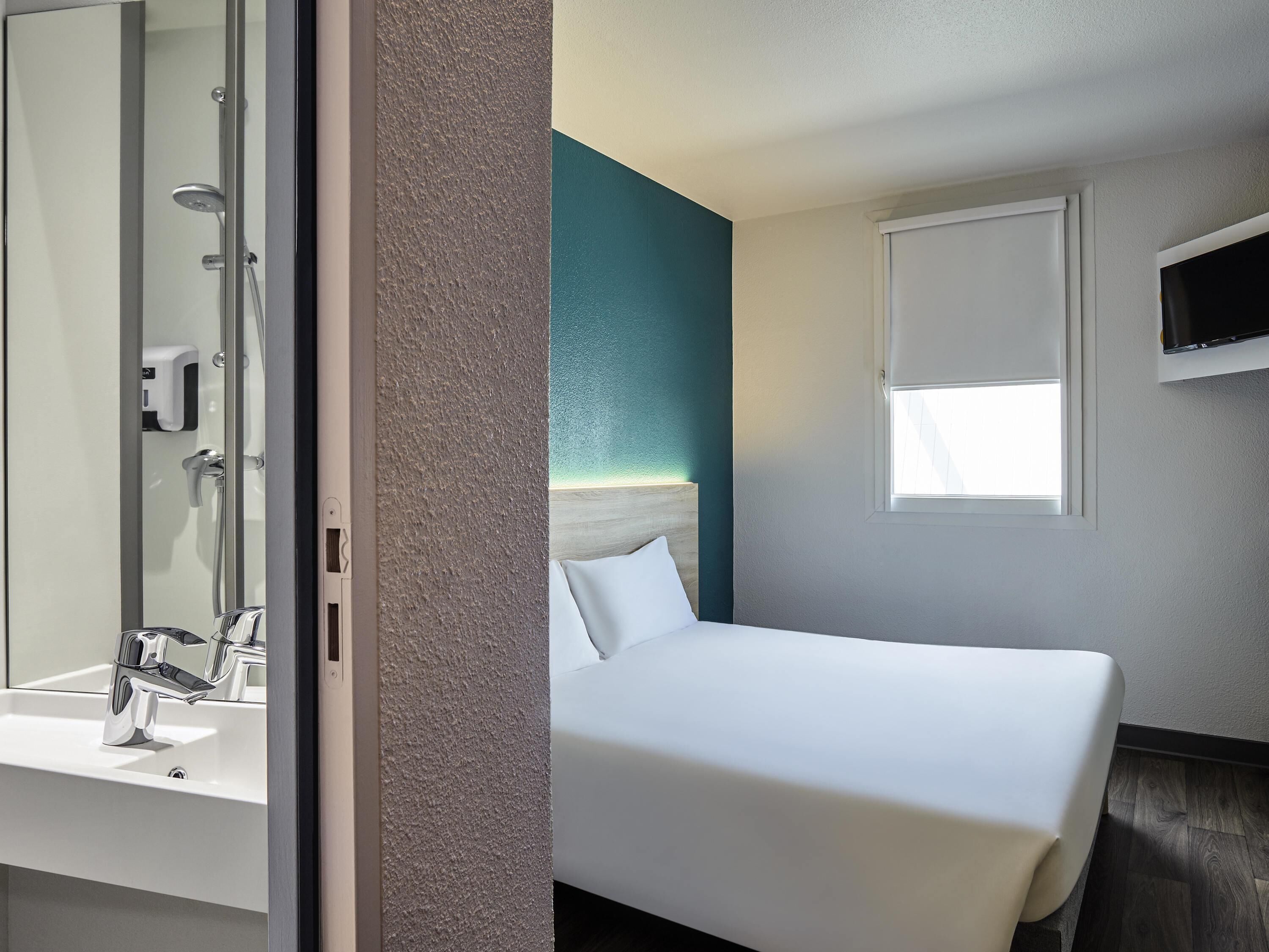 Une chambre d’hôtel comprenant un lit, une salle de bain avec un lavabo et une douche, un téléviseur fixé au mur et une fenêtre.
