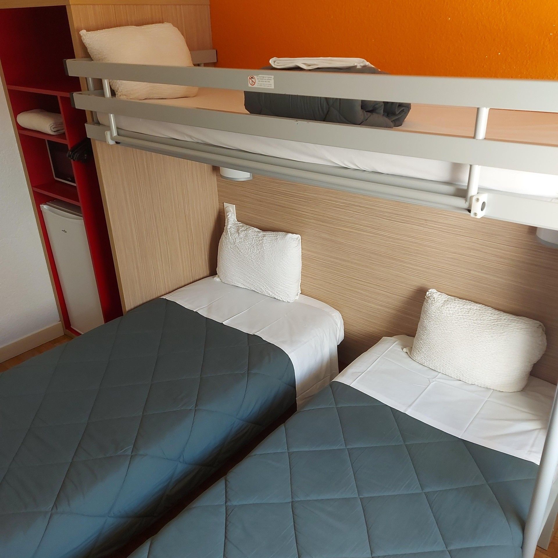 A bunk bed room with two beds, a small desk, and a refrigerator.