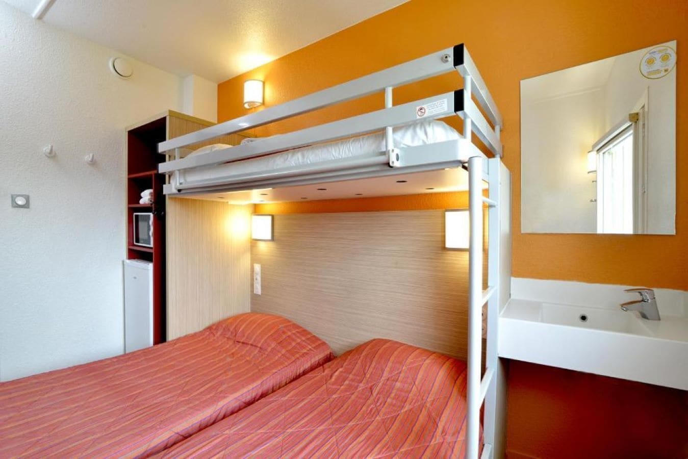 Dormitorio con literas, un lavamanos blanco y un espejo encima.