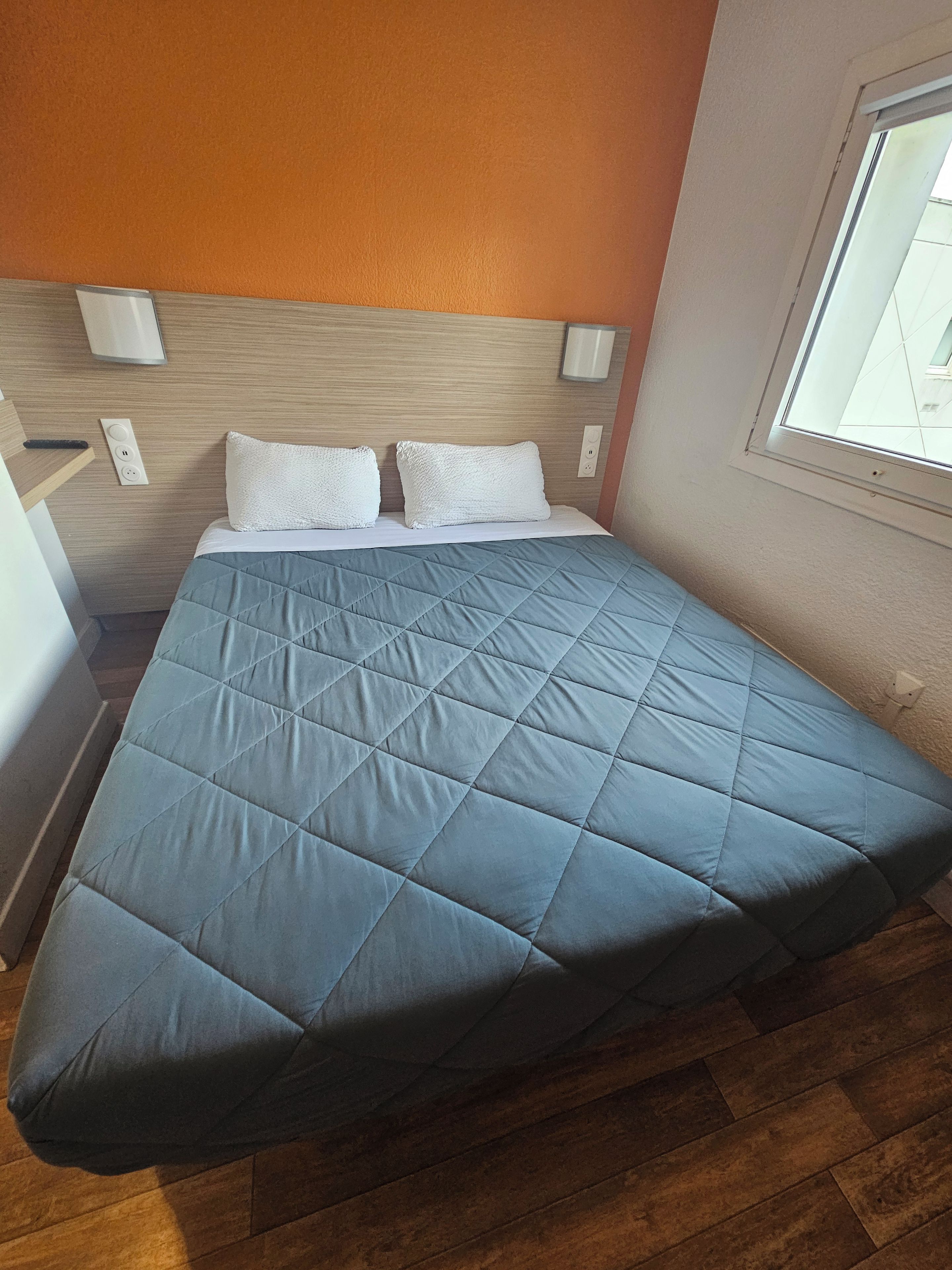 A bed with a quilted blue cover, white pillows, and a wooden headboard.