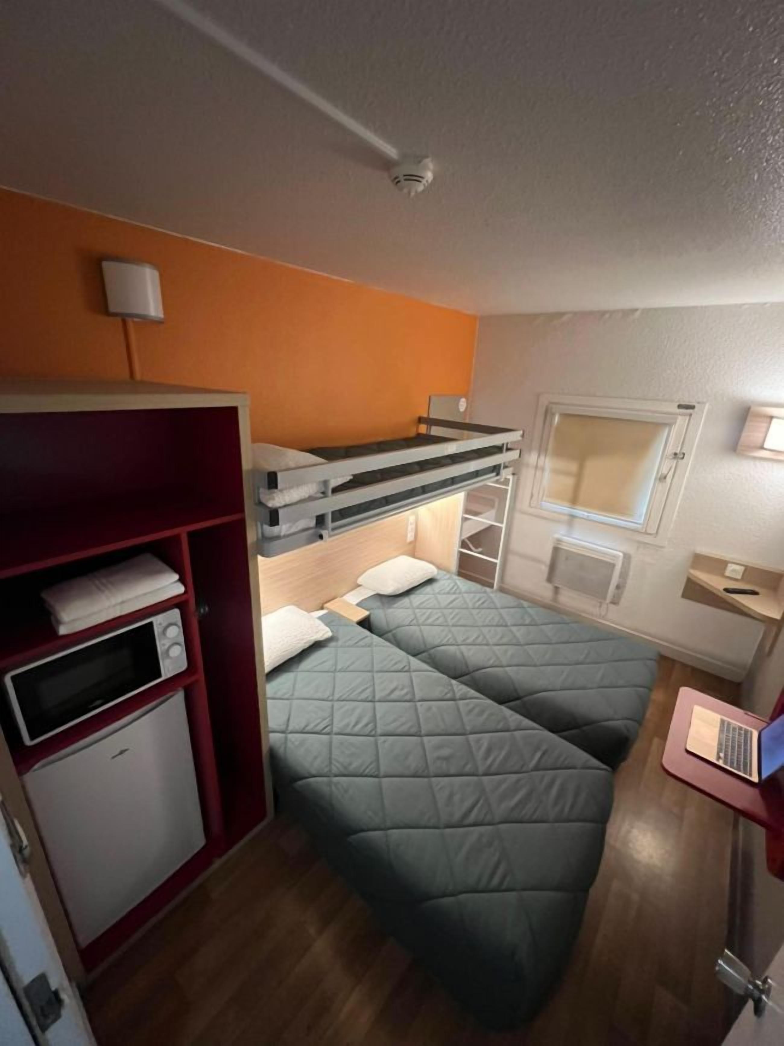 A compact room with bunk beds, a small kitchenette, and a window.