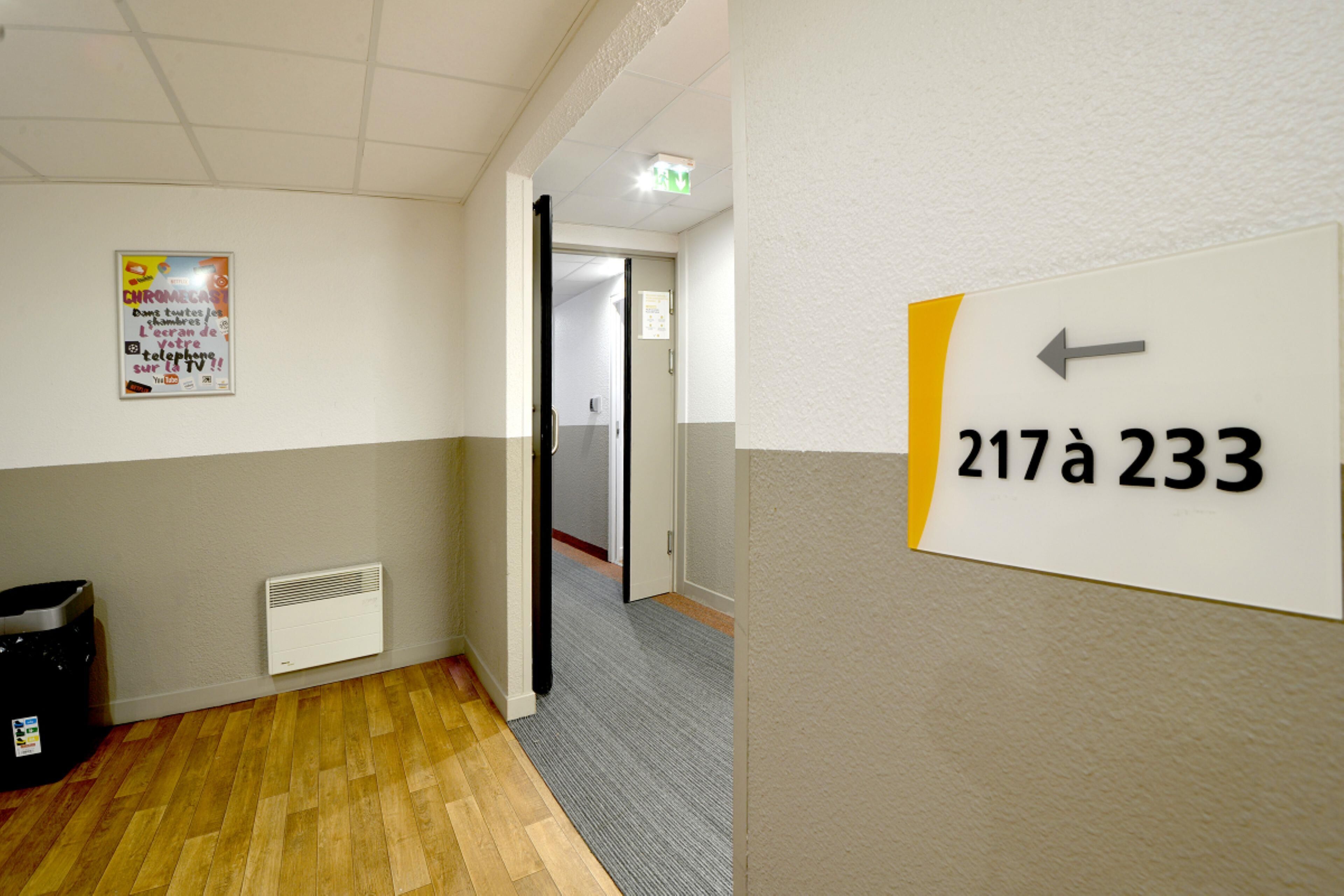 A hallway with a sign indicating room number 217a 233, a poster on the wall, and a radiator.