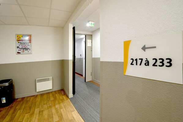 Un pasillo con un cartel que indica las habitaciones 217a y 233, un cartel en la pared y un radiador.