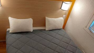 A bed with a quilted grey cover, two pillows, and a headboard with a light fixture.