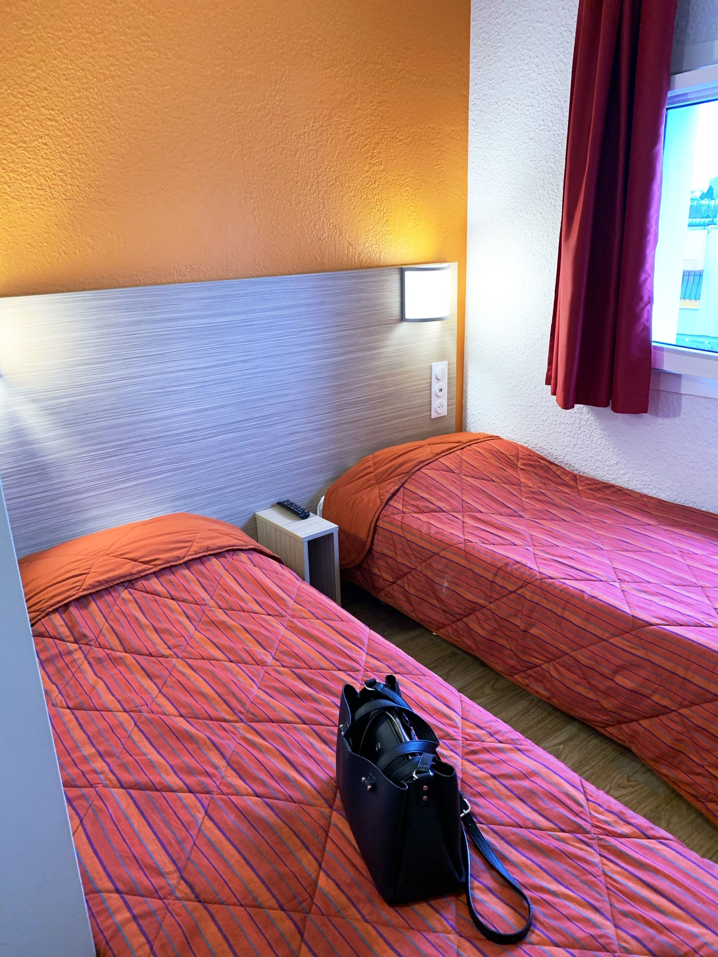 Una habitación de hotel con dos camas, una mesita de noche, una lámpara y una ventana con cortinas.