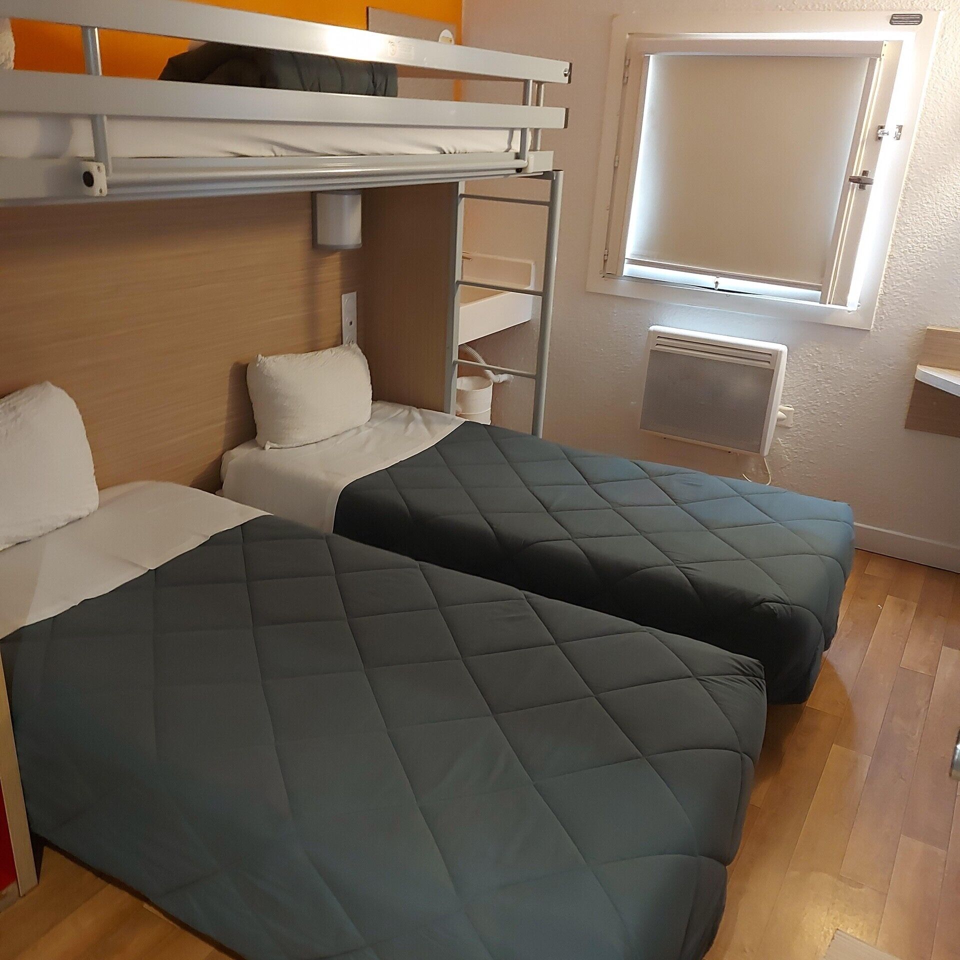 A bunk bed room with a window, a radiator, and a wooden floor.