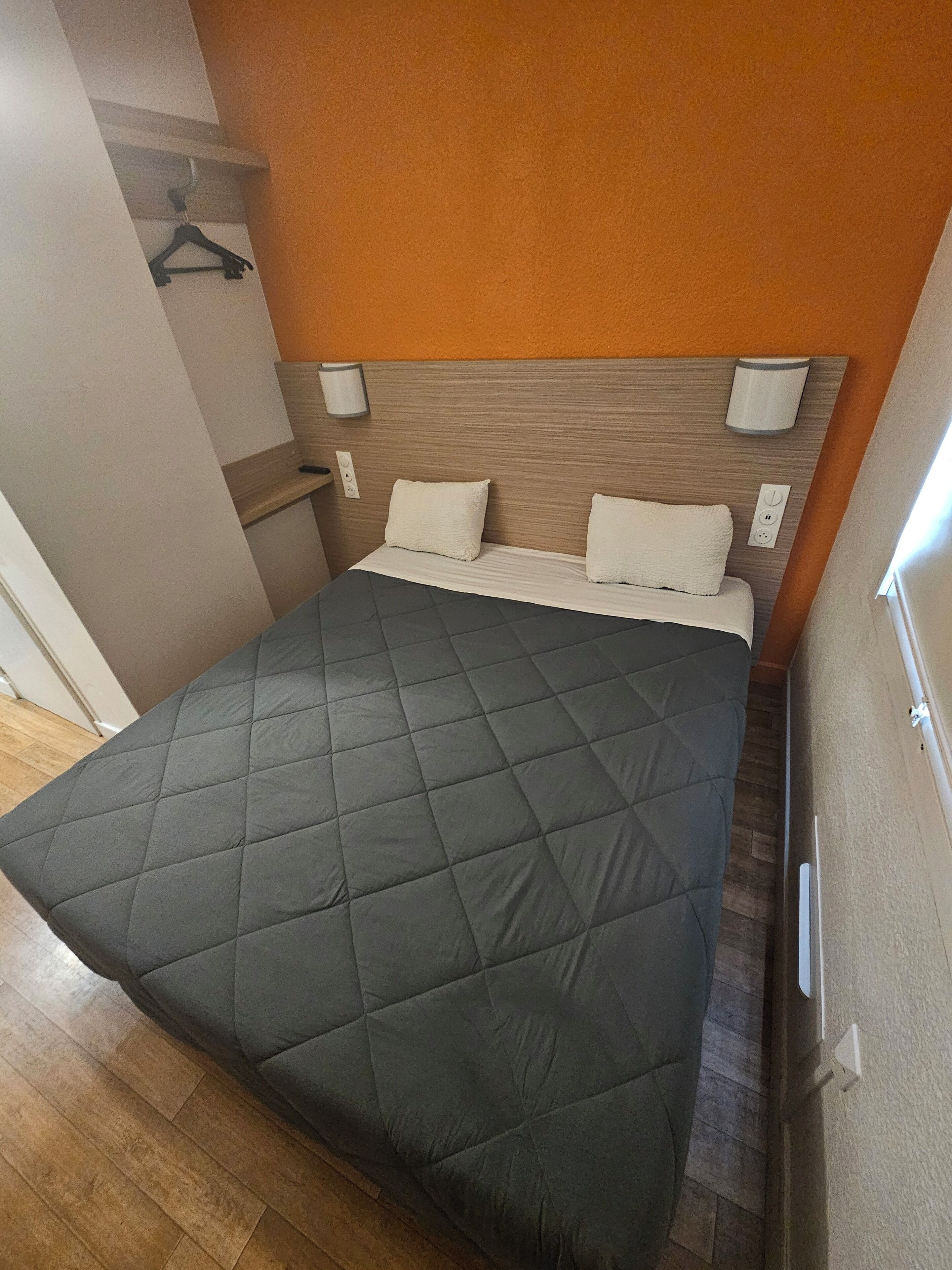A neatly made bed with a dark quilt, a wooden headboard, and two bedside lamps.