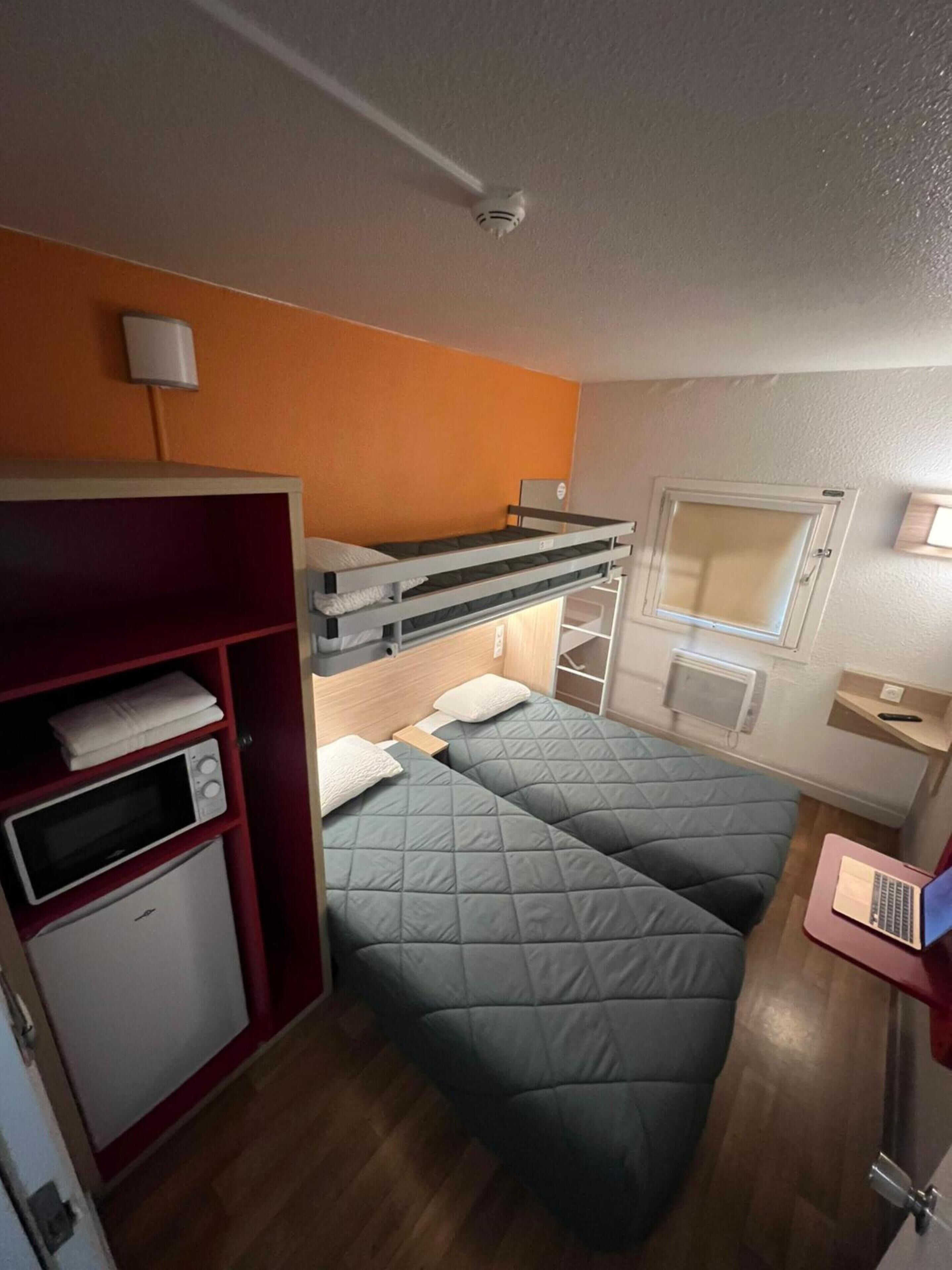 Een kleine kamer met een stapelbed, een kitchenette en een raam.
