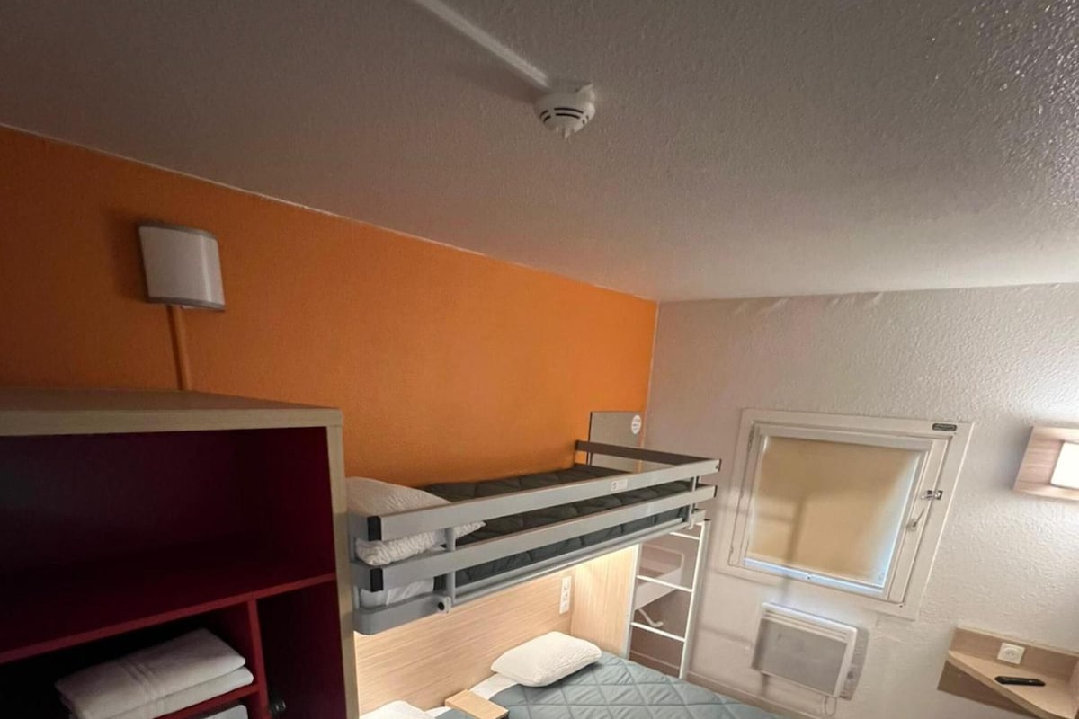 Une petite pièce comprenant un lit superposé, un coin cuisine et une fenêtre.