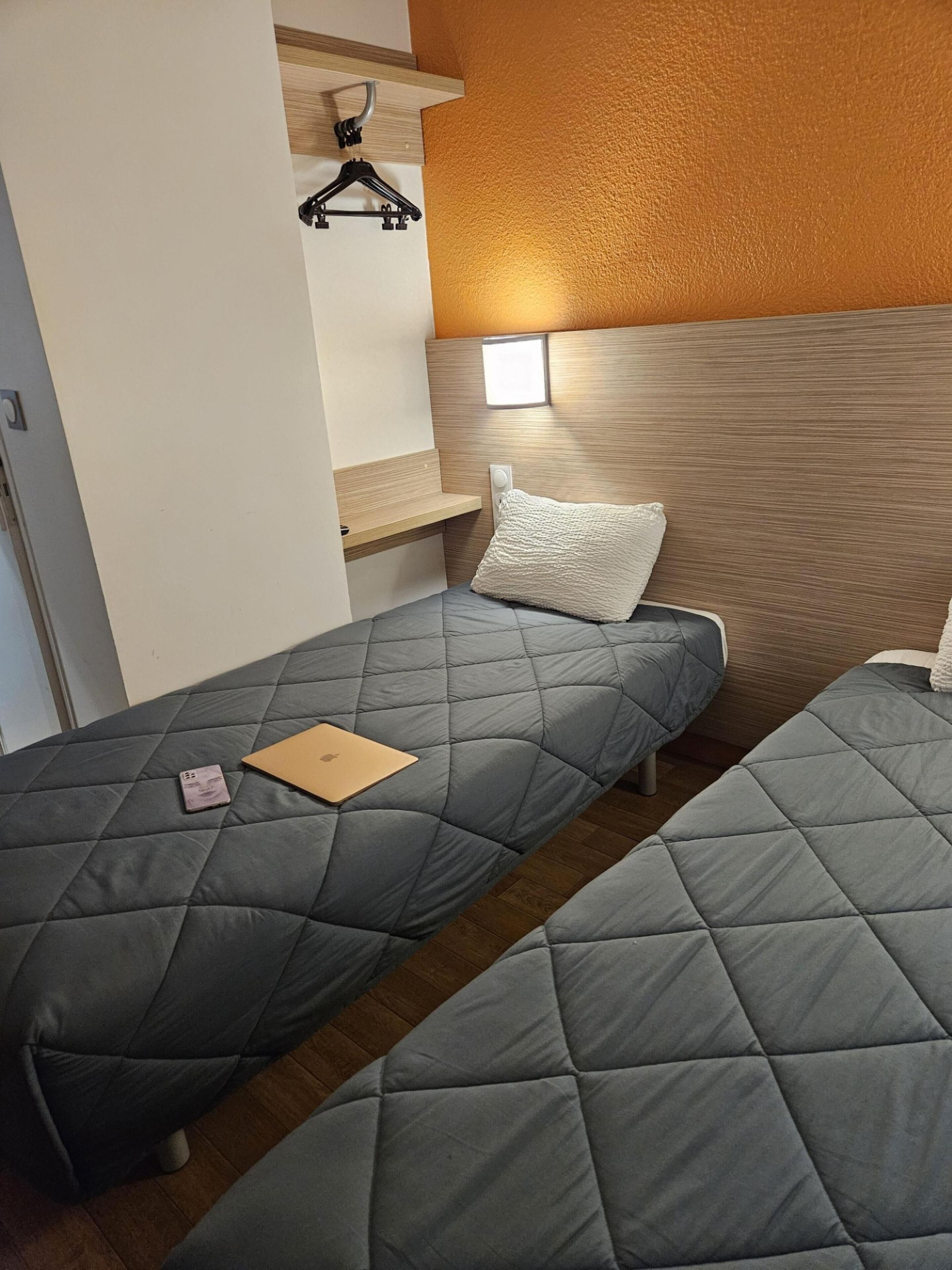 Ein Schlafzimmer mit zwei Einzelbetten, einem Holzkopfteil, einer kleinen Ablage und einem Kleiderhaken.