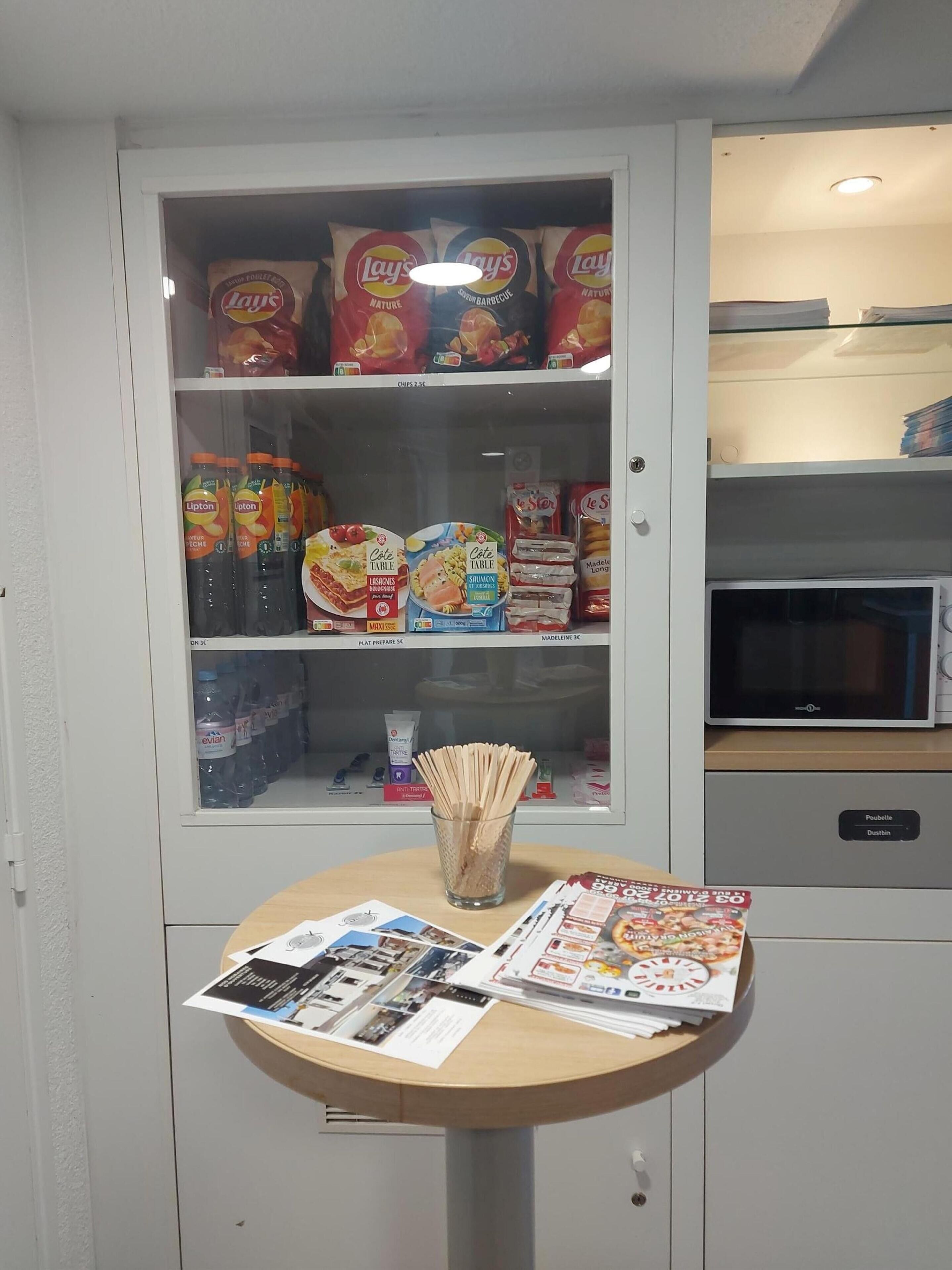 Eine Küchenzeile mit einer Mikrowelle, einem Vorratsschrank voller Snacks, Flaschenwasser und einem Tisch mit Zeitschriften.