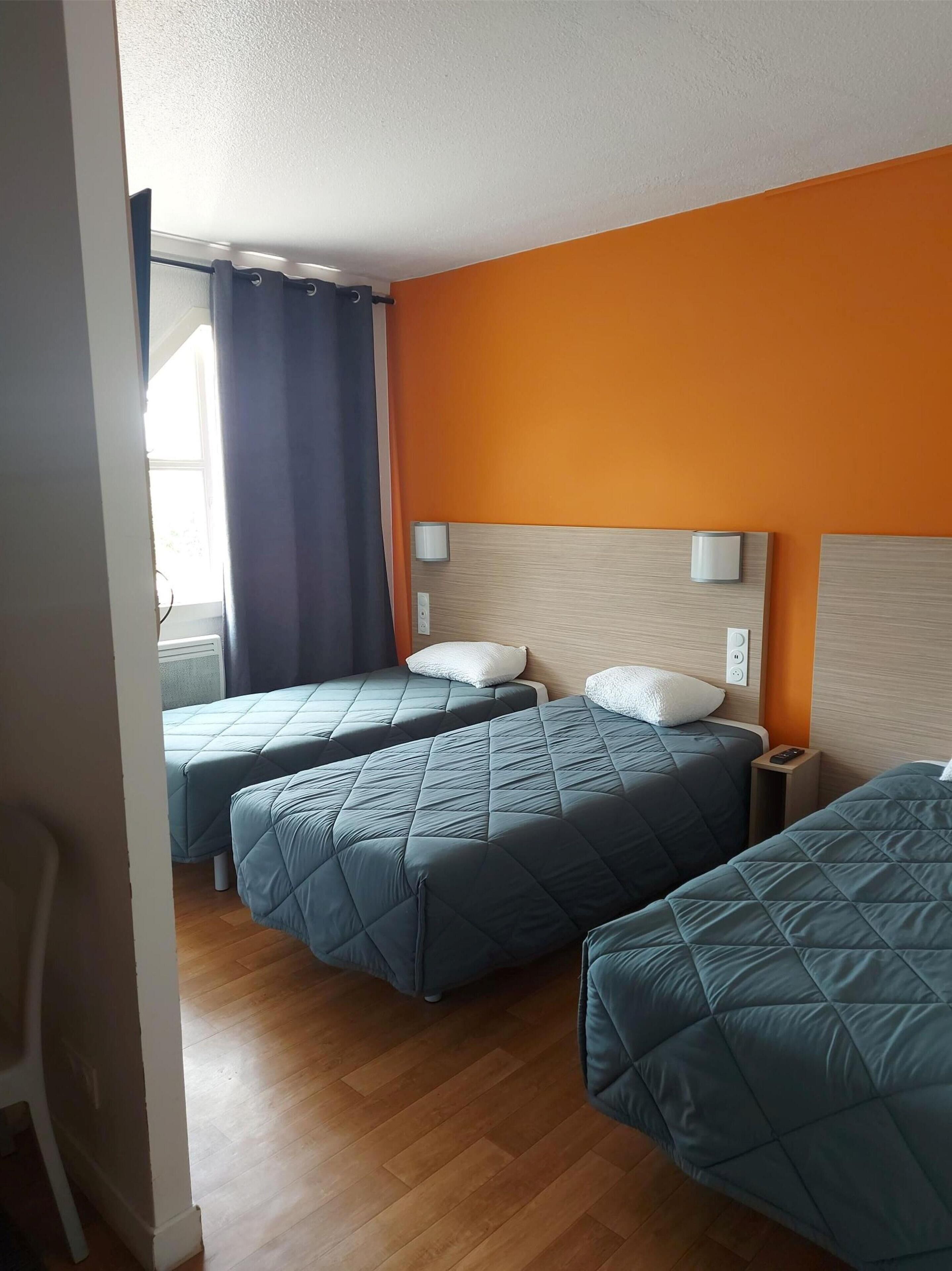Camera d'albergo con due letti, pavimento in legno e finestra con tende.