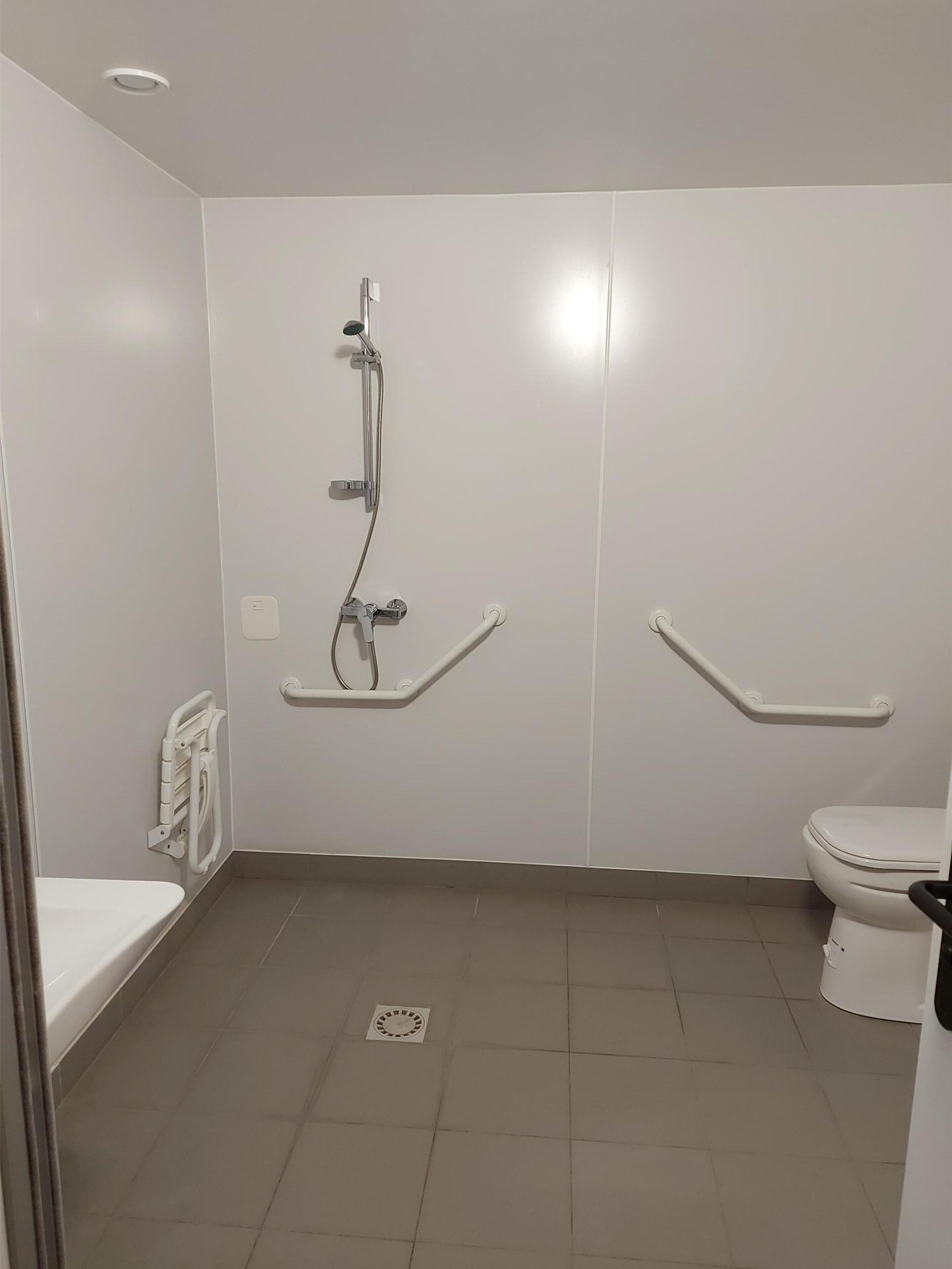 A bathroom with a shower, toilet, and grab bars.