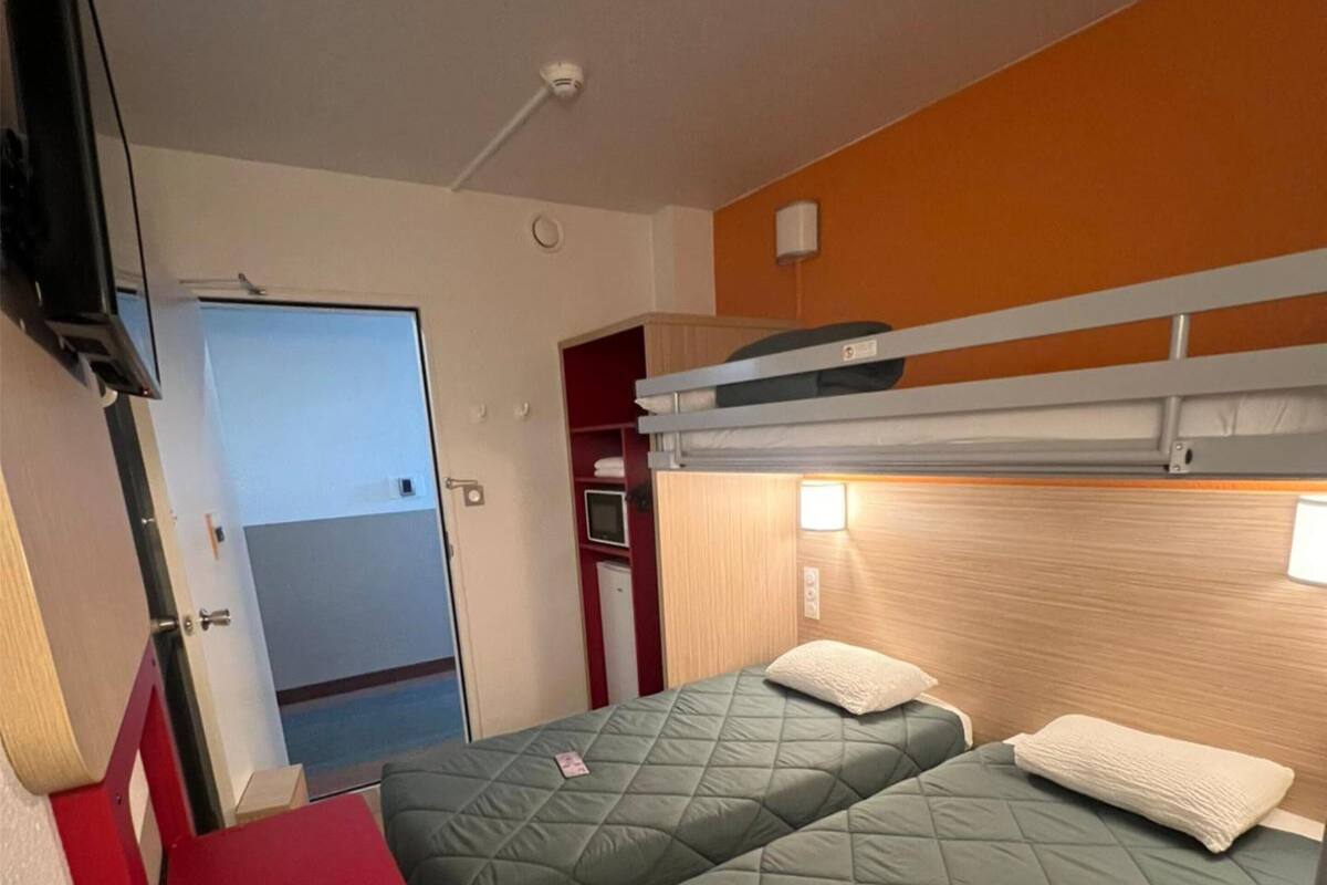 Une chambre d’hôtel de taille modeste, équipée de deux lits, d’une télévision et d’un petit bureau.