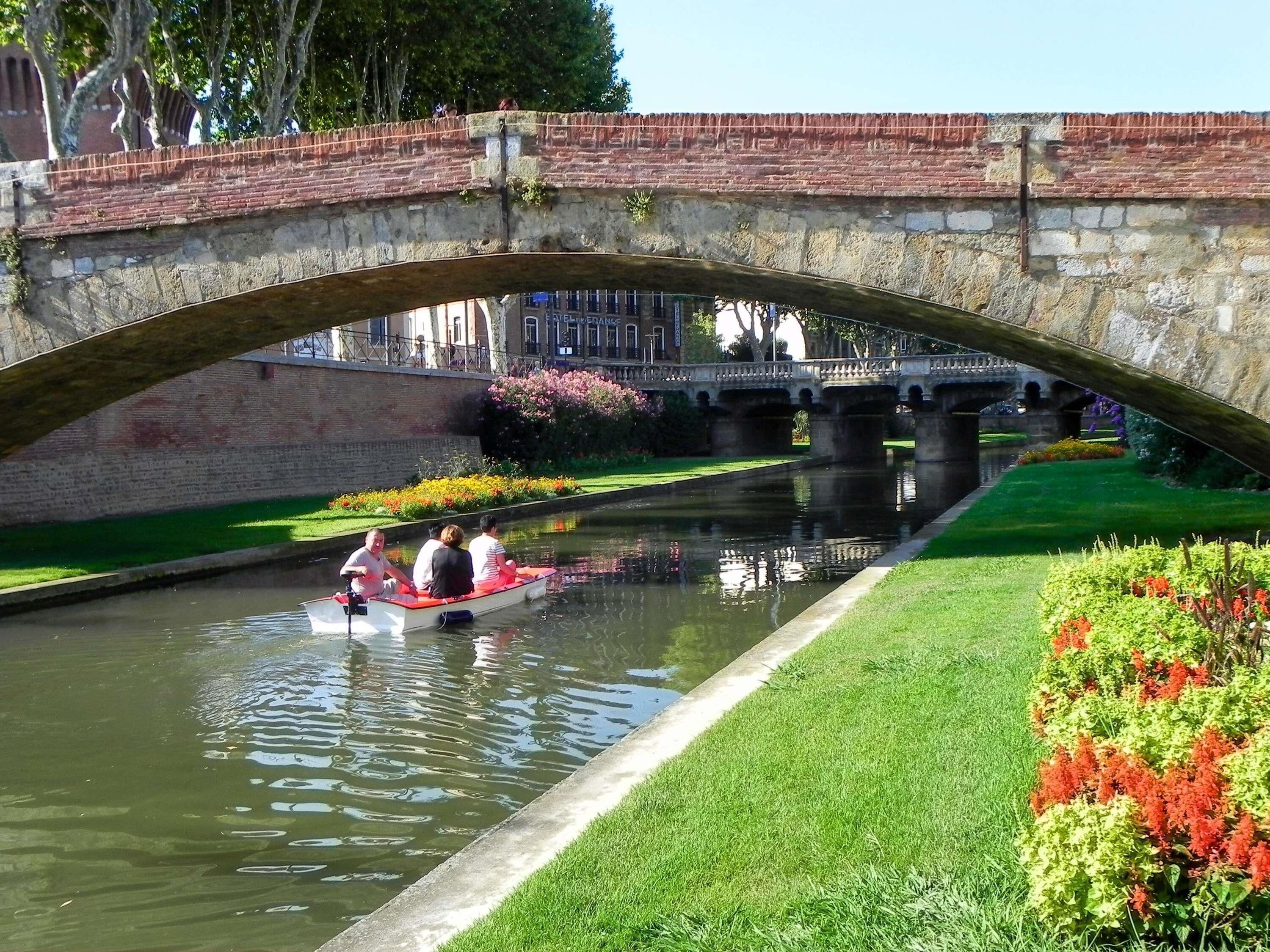 A stone bridge over a canal with a boat carrying passengers.