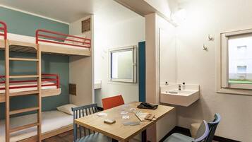 Una cama individual superpuesta, una mesa con sillas, una ventana y un lavamanos pequeño.