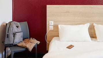 Ein Hotelzimmer mit einem hölzernen Kopfteil, einem Bett mit weißer Bettwäsche, einem grauen Sessel und einem Nachttisch aus Holz.