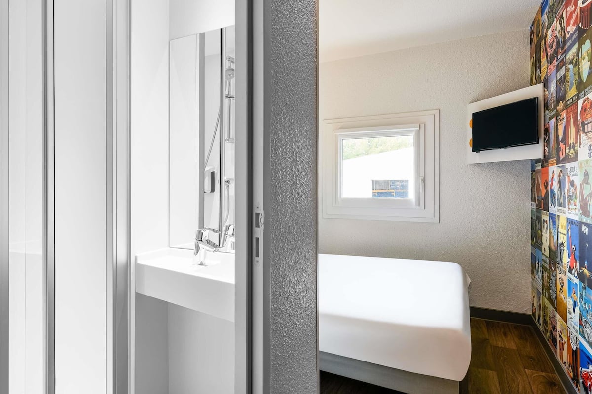 Un baño moderno con cabina de ducha de vidrio, lavamanos blanco y un televisor montado en la pared.