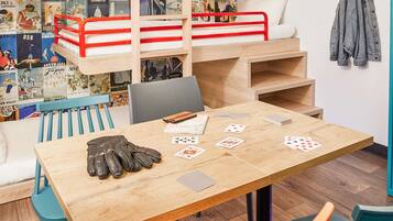 A cozy room with a bunk bed, a wooden table with playing cards, and a wall decorated with vintage travel posters.