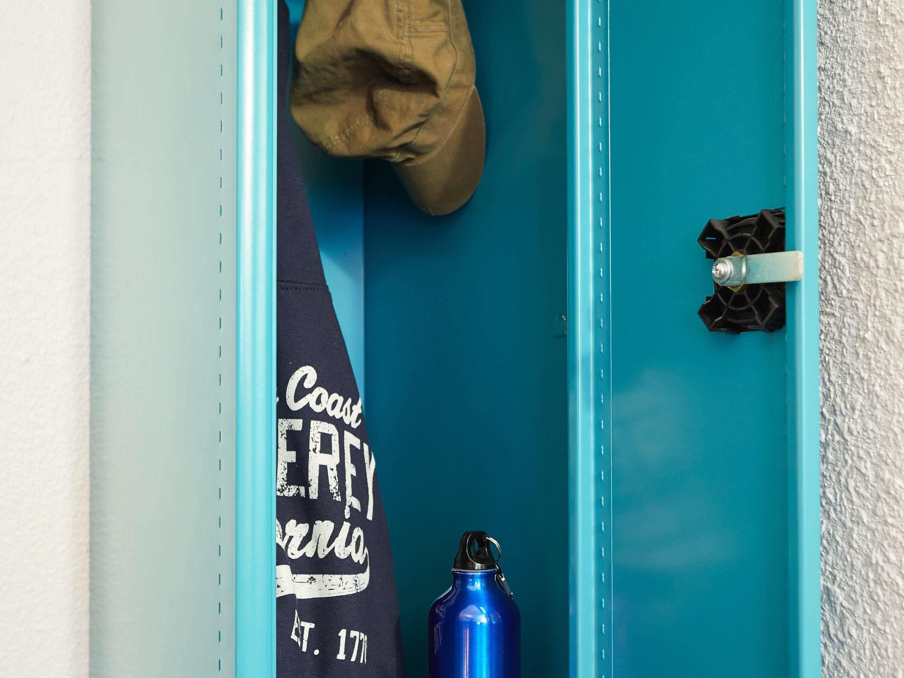A teal door with a towel hanging on the inside handle and a blue water bottle placed on the floor.