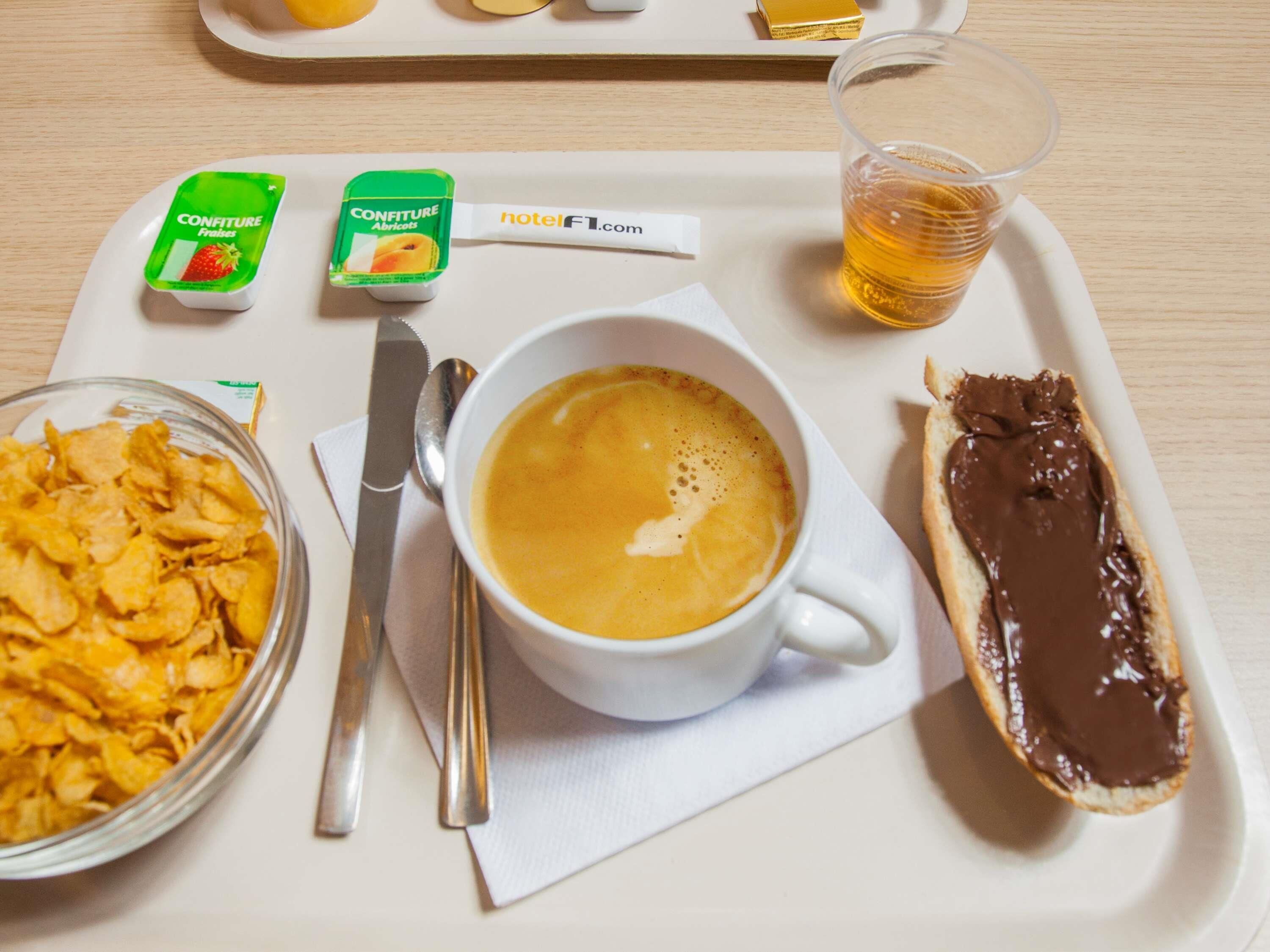 A breakfast tray with a cup of coffee, a bowl of cereal, a pastry with chocolate spread, and two containers of confiture.