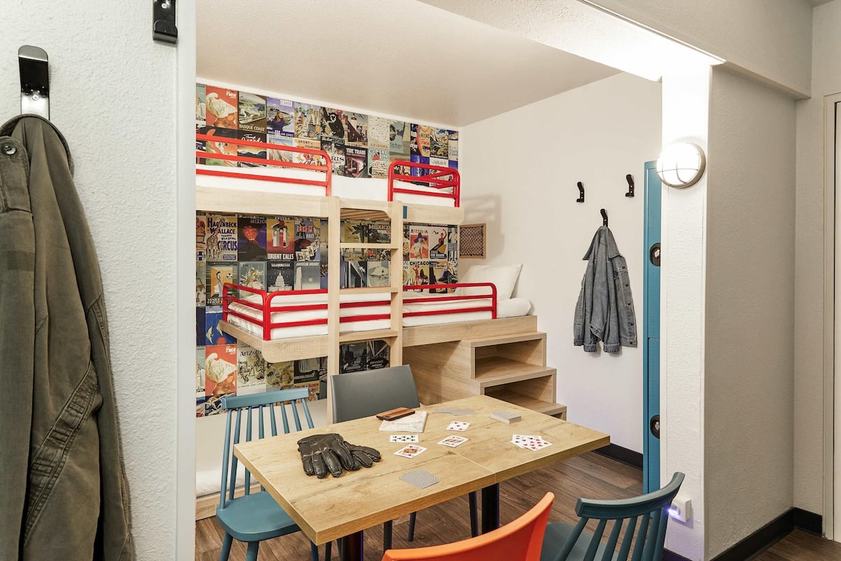 A compact room with a bunk bed, a small table with playing cards, and a wall decorated with travel posters.