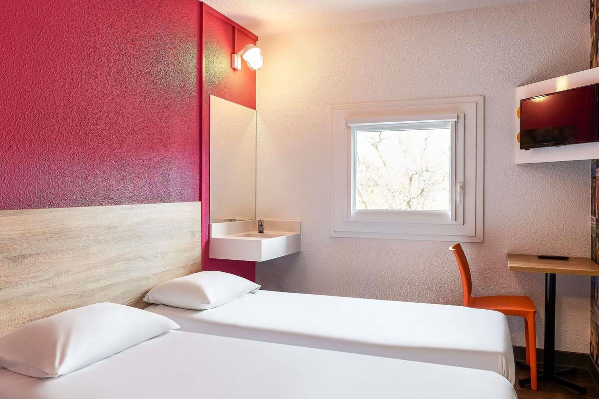 A hotel room with a bed, a window, a desk, and a chair.