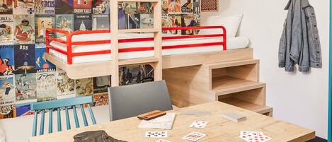 A bunk bed with posters, a table with playing cards, a chair, and a jacket hanging on the wall.