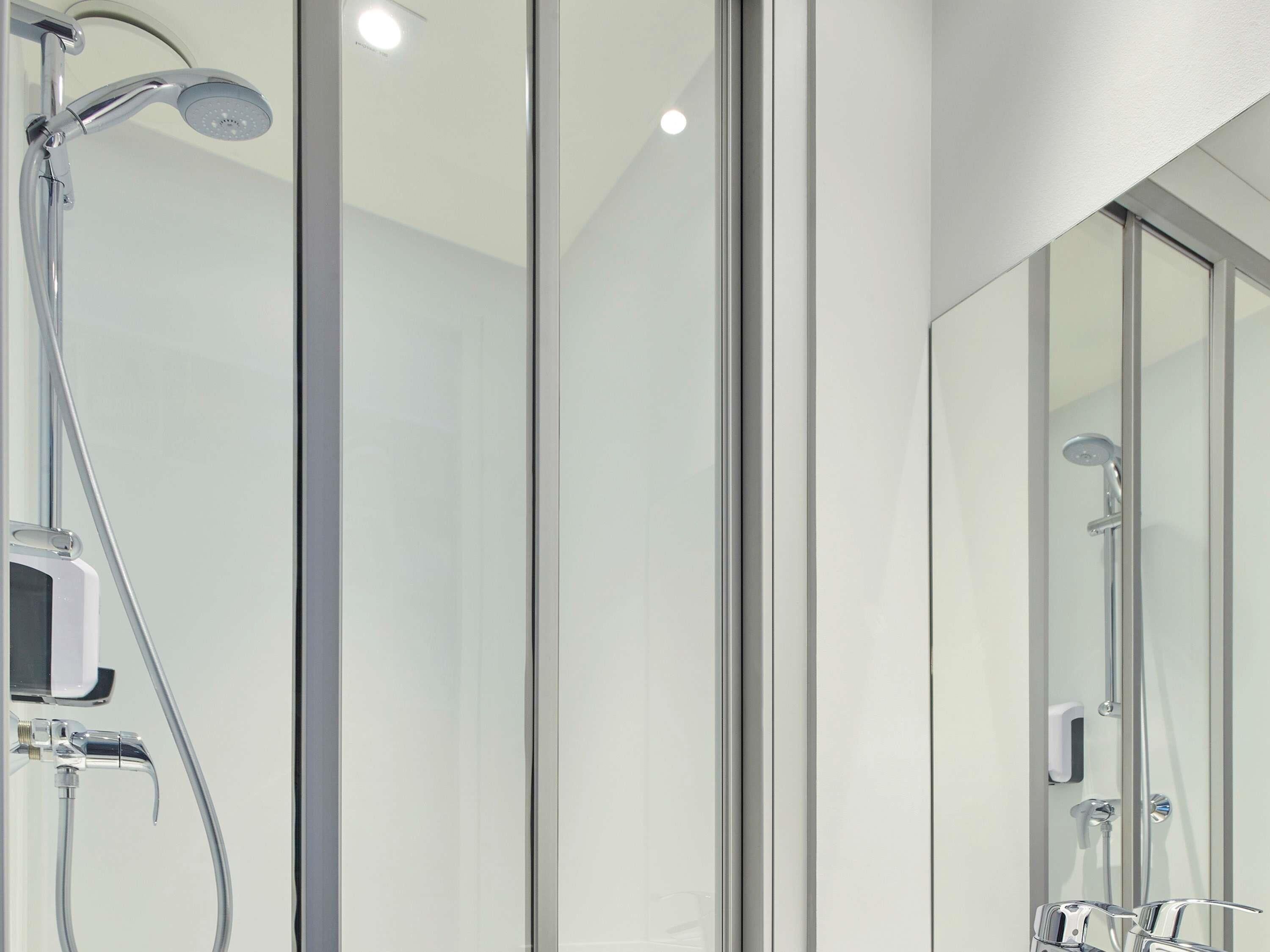 Un baño moderno con cabina de ducha de vidrio, cabezal de ducha de mano y grifo empotrado.