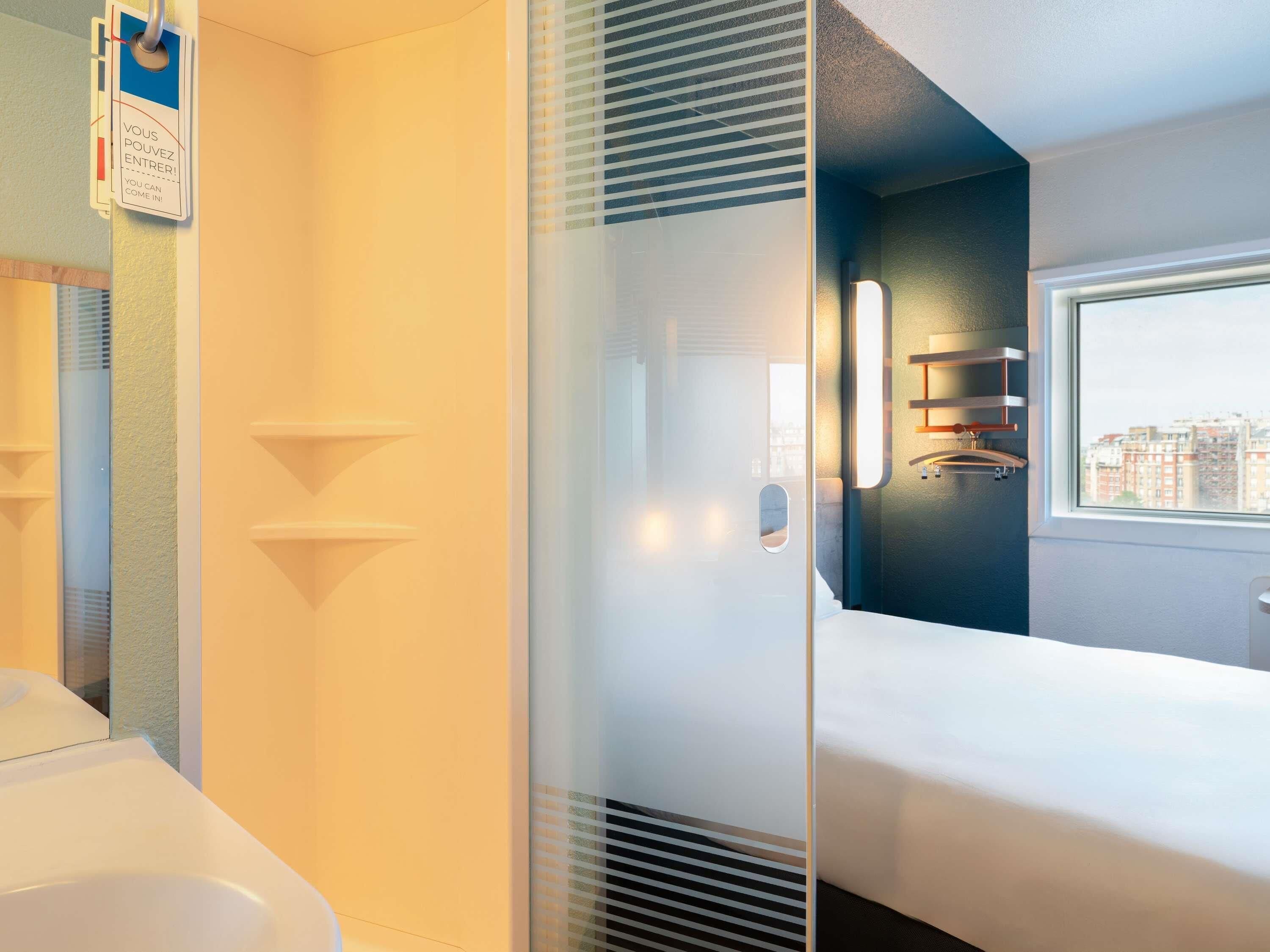 Une chambre d’hôtel comprenant un lit, une fenêtre donnant sur la ville, une salle de bain avec des toilettes et un porte-serviettes fixé au mur.