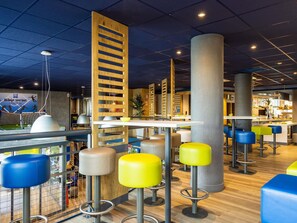 Un espacio interior moderno con techos altos, un muro con temática deportiva y varias áreas de estar con taburetes y mesas.