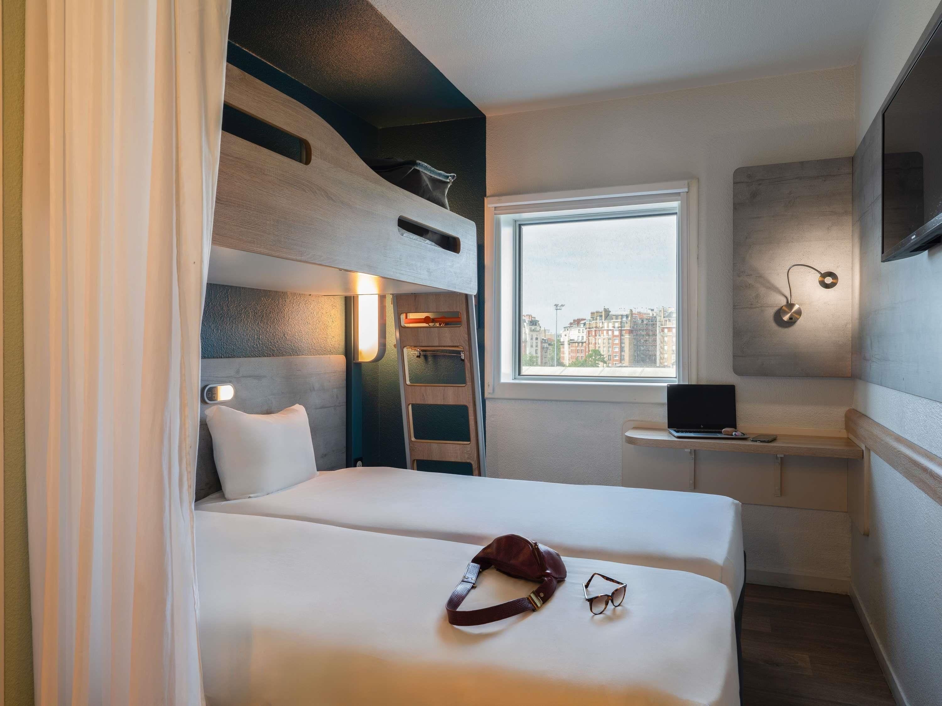 Une chambre d’hôtel de taille réduite, comprenant un lit, un bureau et une fenêtre donnant sur la ville.