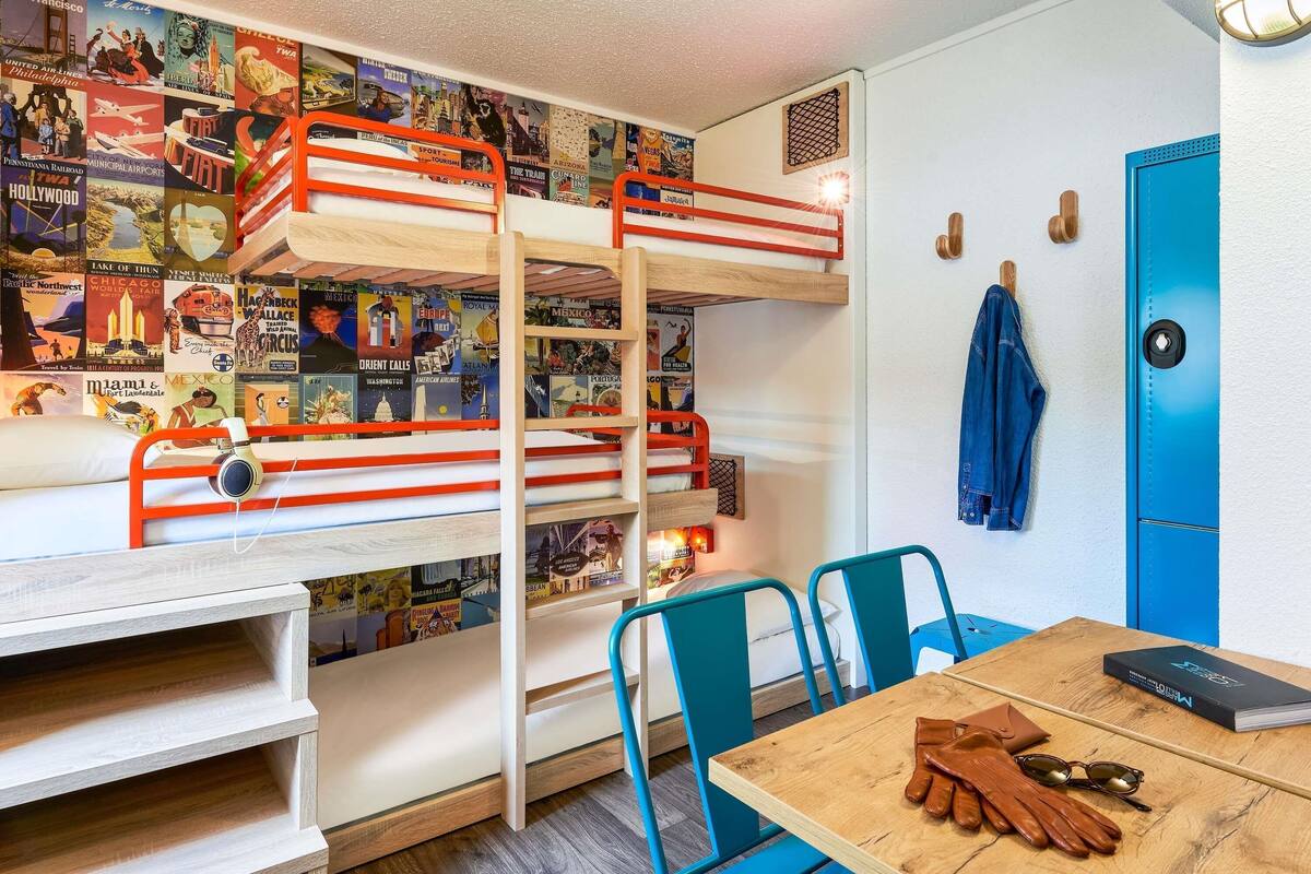 A bunk bed with a travel-themed wall, a desk, a chair, and a table with a book and gloves.