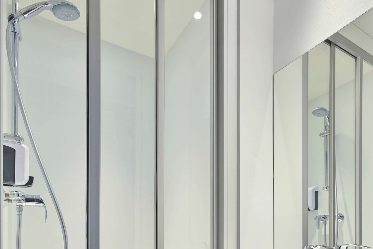 A modern bathroom with a glass shower enclosure, a handheld showerhead, and a wall-mounted faucet.