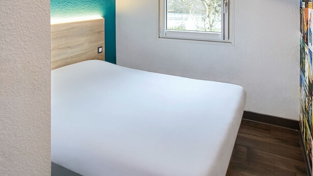 A bathroom with a white bathtub, a wooden headboard, and a window with a view of trees. - hotelF1 Clermont-Ferrand East (Clermont-Ferrand)