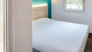 Relax in this serene space with a comfortable bed against a wall, offering a view of the outdoors through the window.