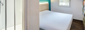 A bathroom with a white bathtub, a wooden headboard, and a window with a view of trees. - hotelF1 Clermont-Ferrand East (Clermont-Ferrand)