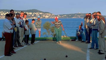 Un groupe de personnes joue à la pétanque sur un terrain aménagé, avec une vue pittoresque sur le bord de l’eau en arrière-plan.