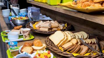 Un buffet proposant une variété d’aliments, notamment du pain, des pâtisseries, des fruits et des boissons.