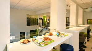 A modern hotel dining area with a long counter, seating, and a staircase in the background. - ibis budget Nice Aeroport Promenade des Anglais (Nice)
