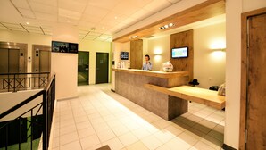 A reception area with a wooden reception desk, a digital screen, and a staircase with a railing. - ibis budget Nice Aeroport Promenade des Anglais (Nice)