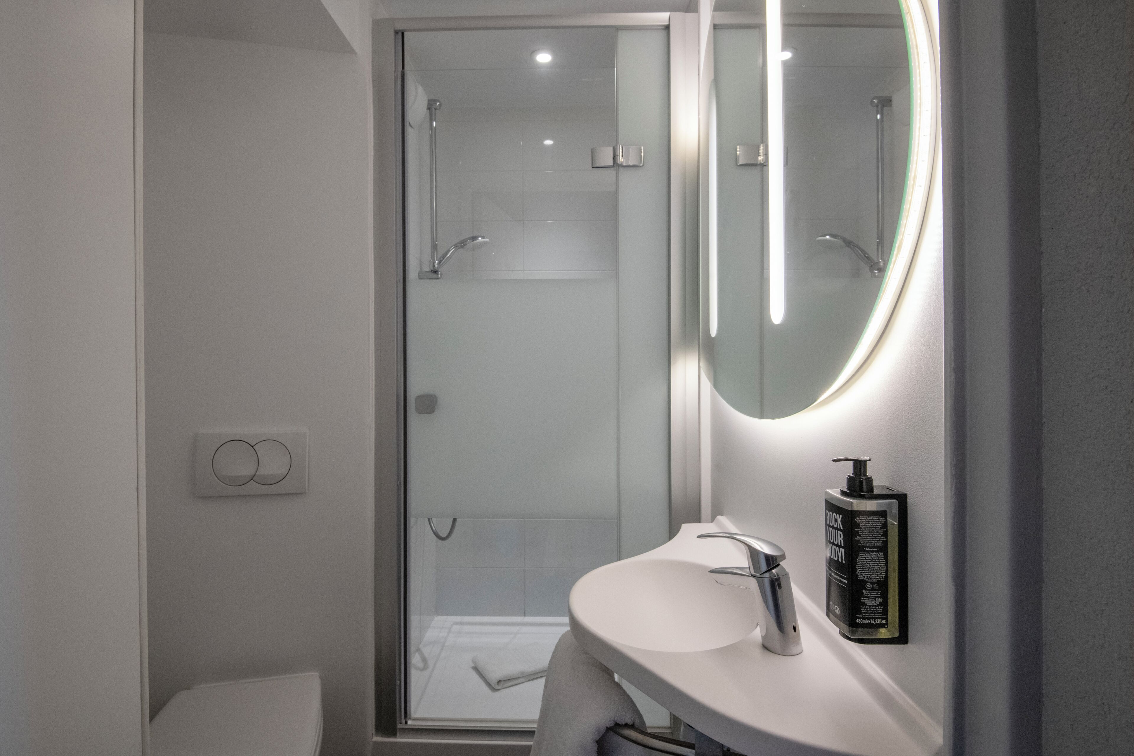 A modern bathroom with a glass-enclosed shower, a white sink, and a mirror with integrated lighting.