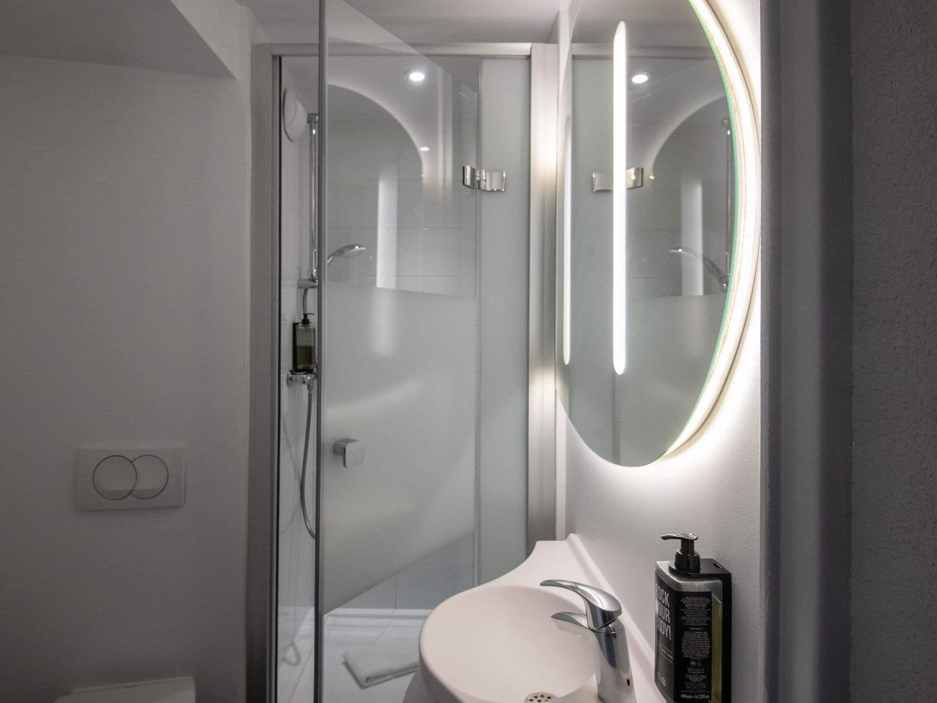 Un baño moderno con ducha de vidrio, lavamanos blanco con un solo grifo y un espejo con iluminación integrada.
