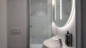 Une salle de bain moderne avec une douche à parois de verre, un lavabo blanc et un miroir doté d’un éclairage intégré.