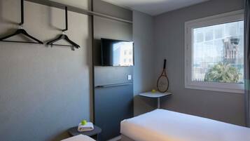 A hotel room with two beds, a TV, a tennis racket, and a window with a city view.