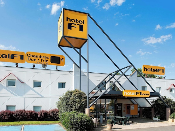 A hotel with a modern design, featuring a prominent 'hotel F1' sign, a covered outdoor seating area, and a pool.